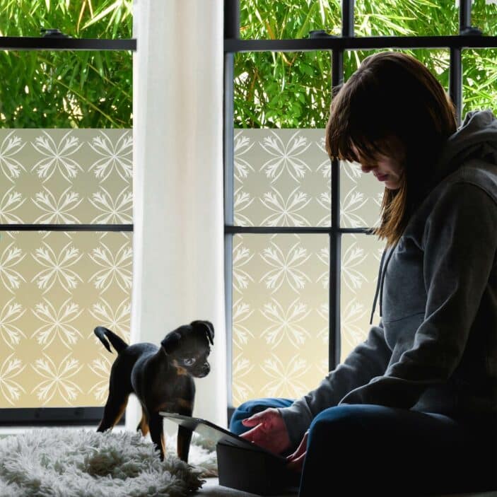 A girl and dog in a bedroom are shielded by privacy film for windows adorned with art deco inspired lillies.